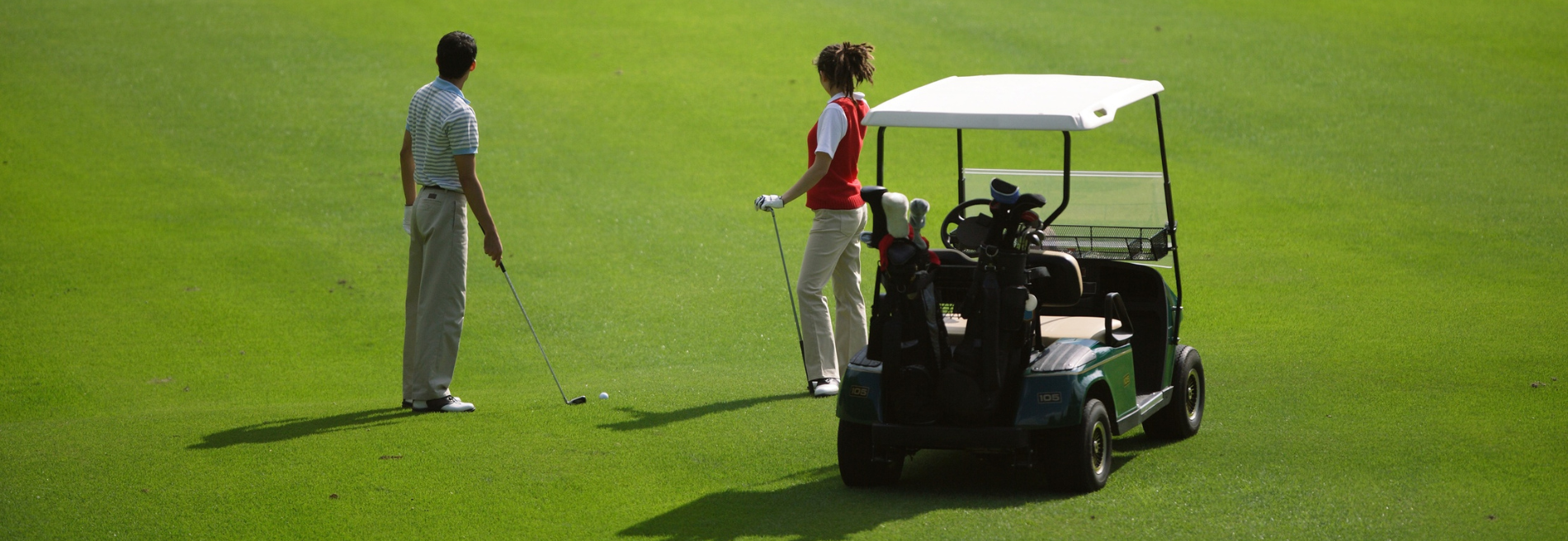 Two golfers, a man and a woman, on a green course with a golf cart, ready to play.